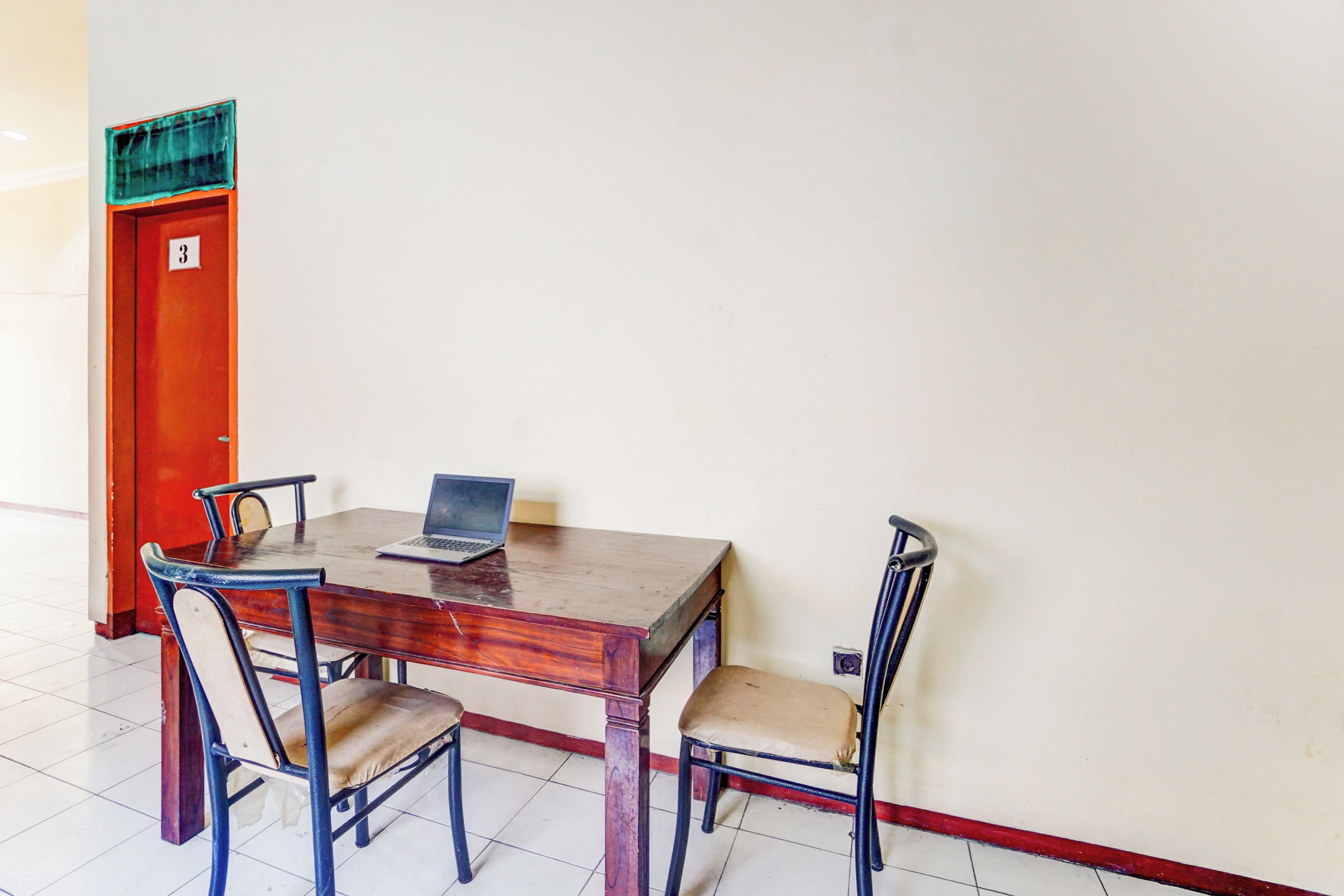 A wooden table with a laptop, four chairs, and a red door with the number 3.