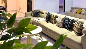 A modern living room with a sofa, a coffee table, and a ceiling with recessed lighting and a chandelier. - DF Blessed Apartment (Abuja)