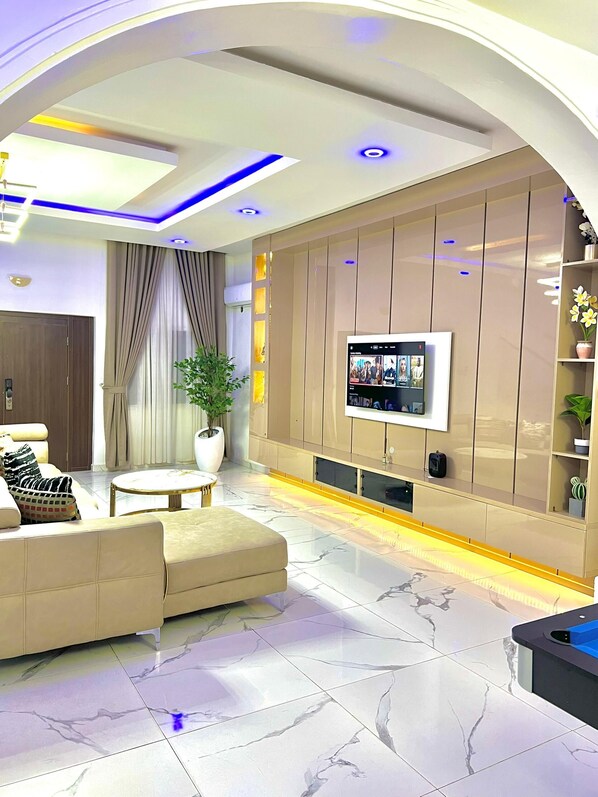 A modern living room with a sofa, a coffee table, a TV mounted on a wooden panel wall, and a potted plant.