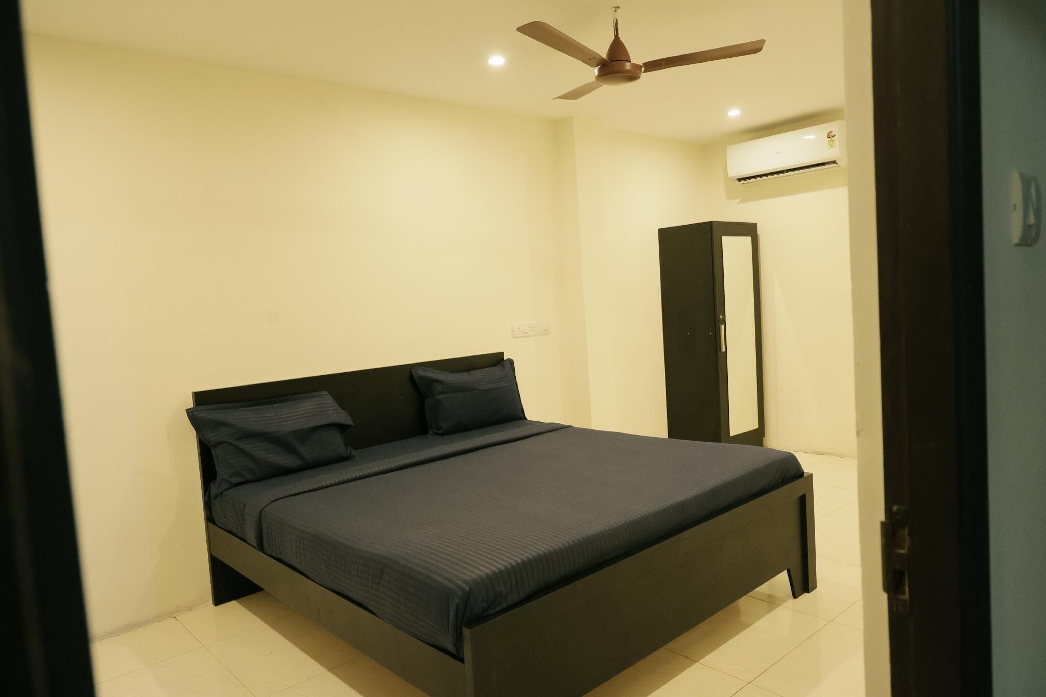 A bedroom with a bed, a ceiling fan, an air conditioning unit, and a wardrobe.