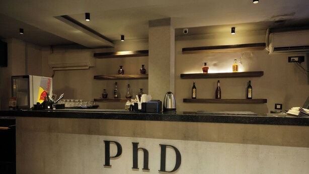 Uma área de bar com balcão exibindo as letras “PhD” e prateleiras com garrafas.