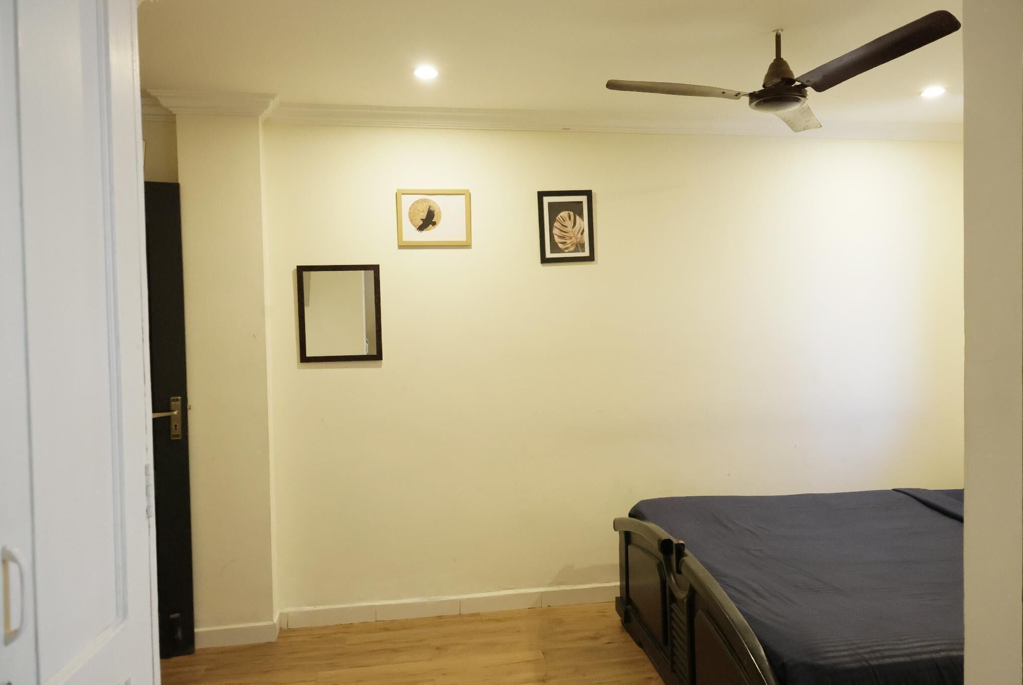 A bedroom with a bed, a ceiling fan, and three framed pictures on the wall.
