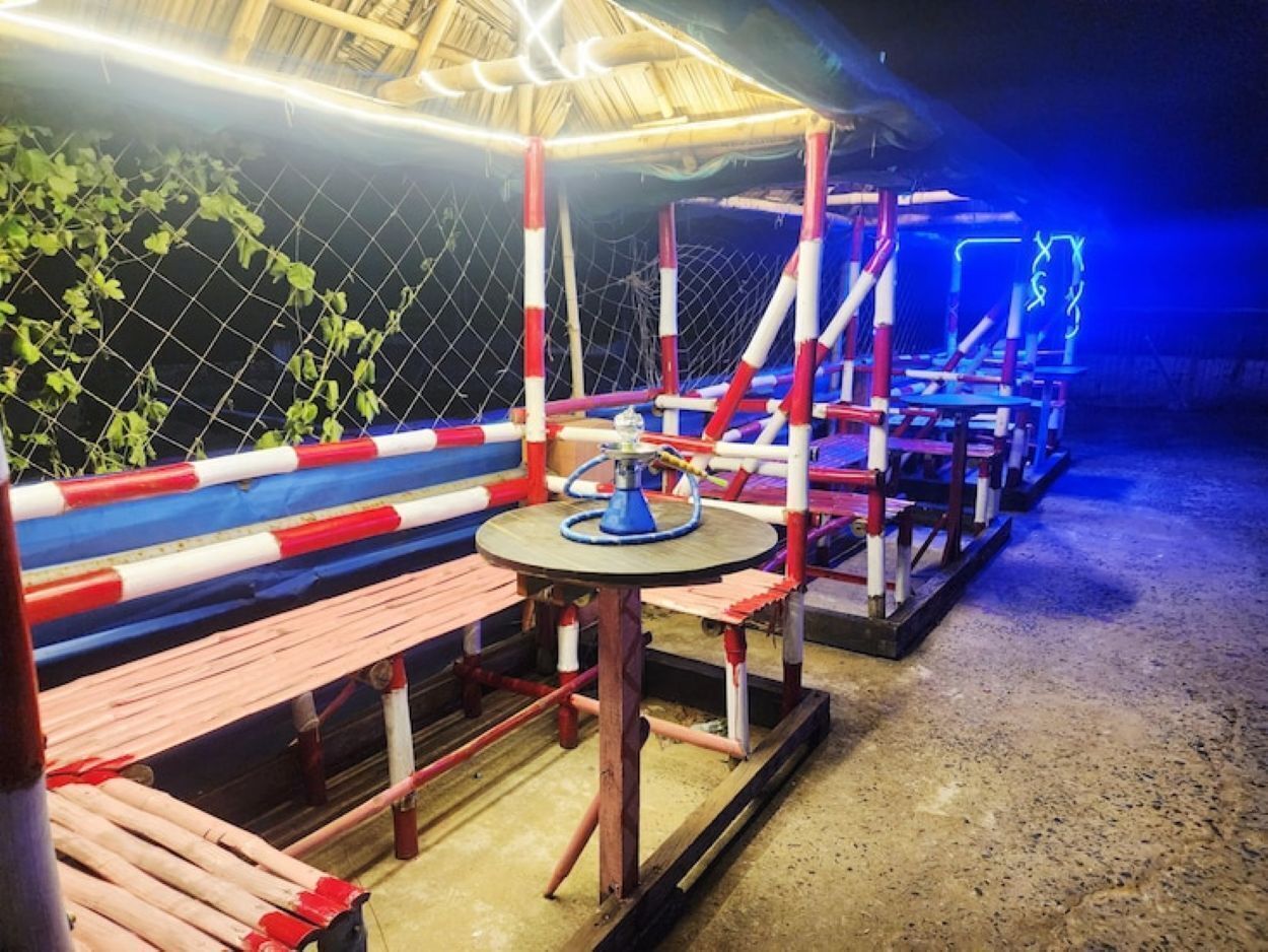 An outdoor seating area with a table and benches, surrounded by a fence and a covered structure.