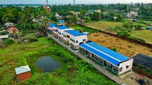 A long building with a blue roof, surrounded by greenery and a small pond. - Resort Garden Retreat (Kanthi)