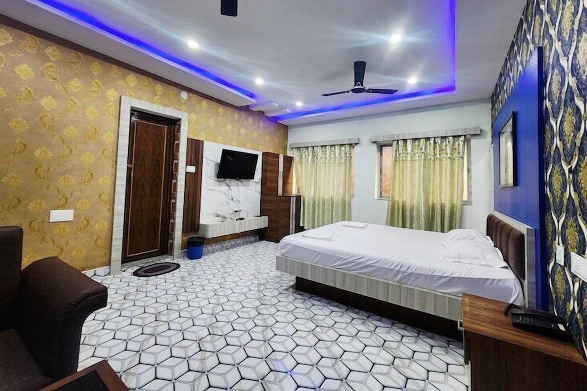 Una habitación de hotel con una cama grande, ventilador de techo, televisor montado en la pared y papel tapiz estampado.