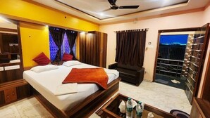 A hotel room with a bed, a desk, a chair, a balcony with a railing, and a ceiling fan. - Resort Garden Retreat (Kanthi)