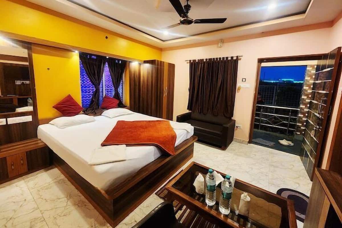 Una habitación de hotel con cama, escritorio, silla, balcón con barandilla y ventilador de techo.