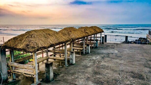 A beachside area with thatched-roof structures and concrete benches. - Resort Garden Retreat (Kanthi)