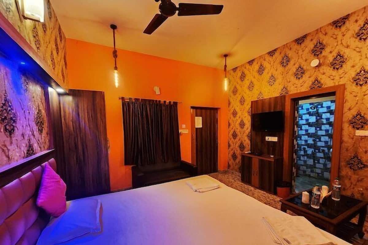 Habitación de hotel con cama, ventilador de techo, televisor y baño con pared decorada.