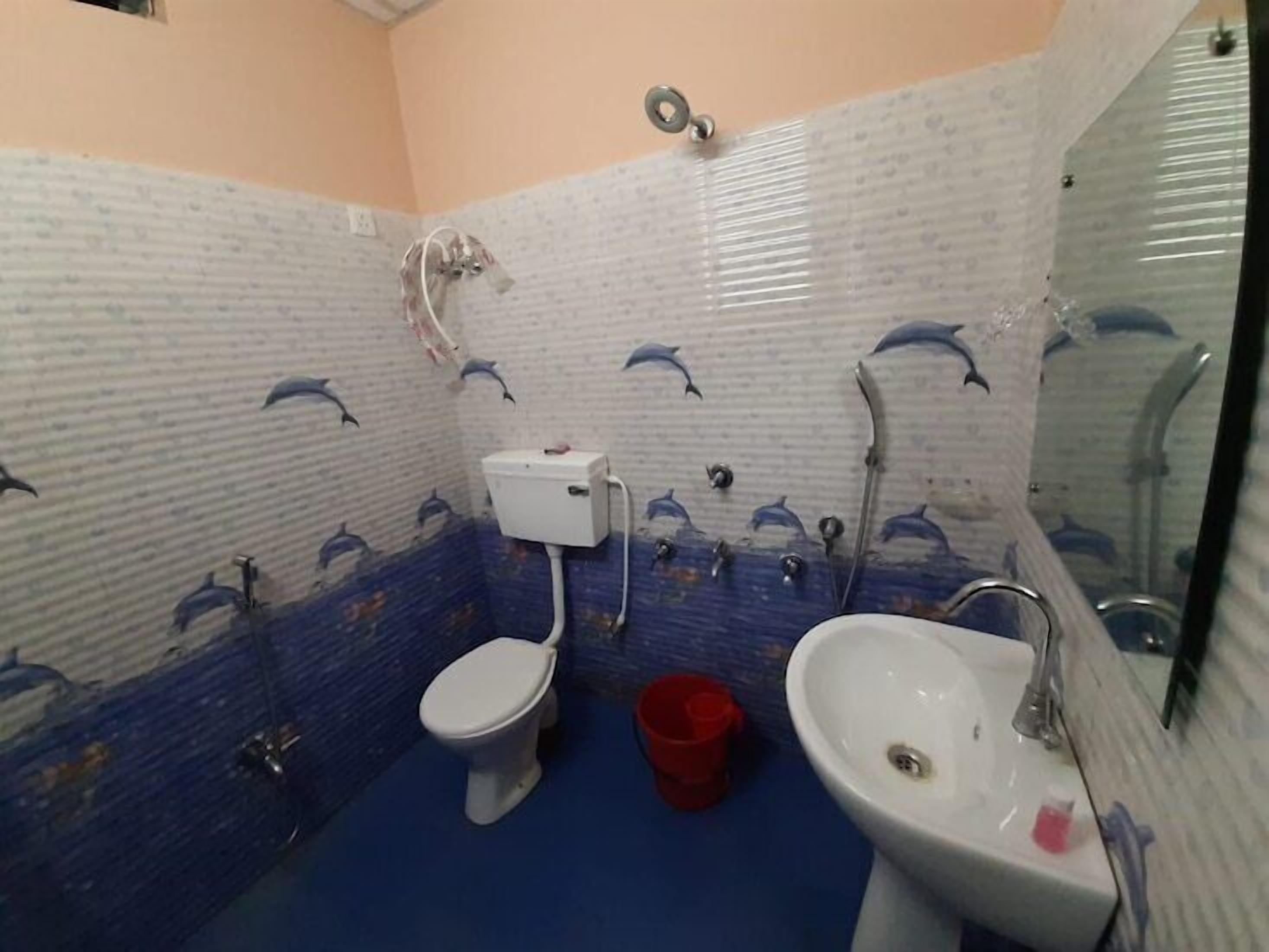 Casa de banho com sanita, lavatório e chuveiro. Os azulejos das paredes apresentam um padrão com motivos de golfinhos.