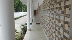 A corridor with white columns, a patterned wall, and potted plants. - Resort Garden Retreat (Kanthi)