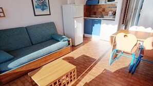 Un espace de vie compact comprenant un canapé, une table en bois, une chaise et, au fond, un coin cuisine.