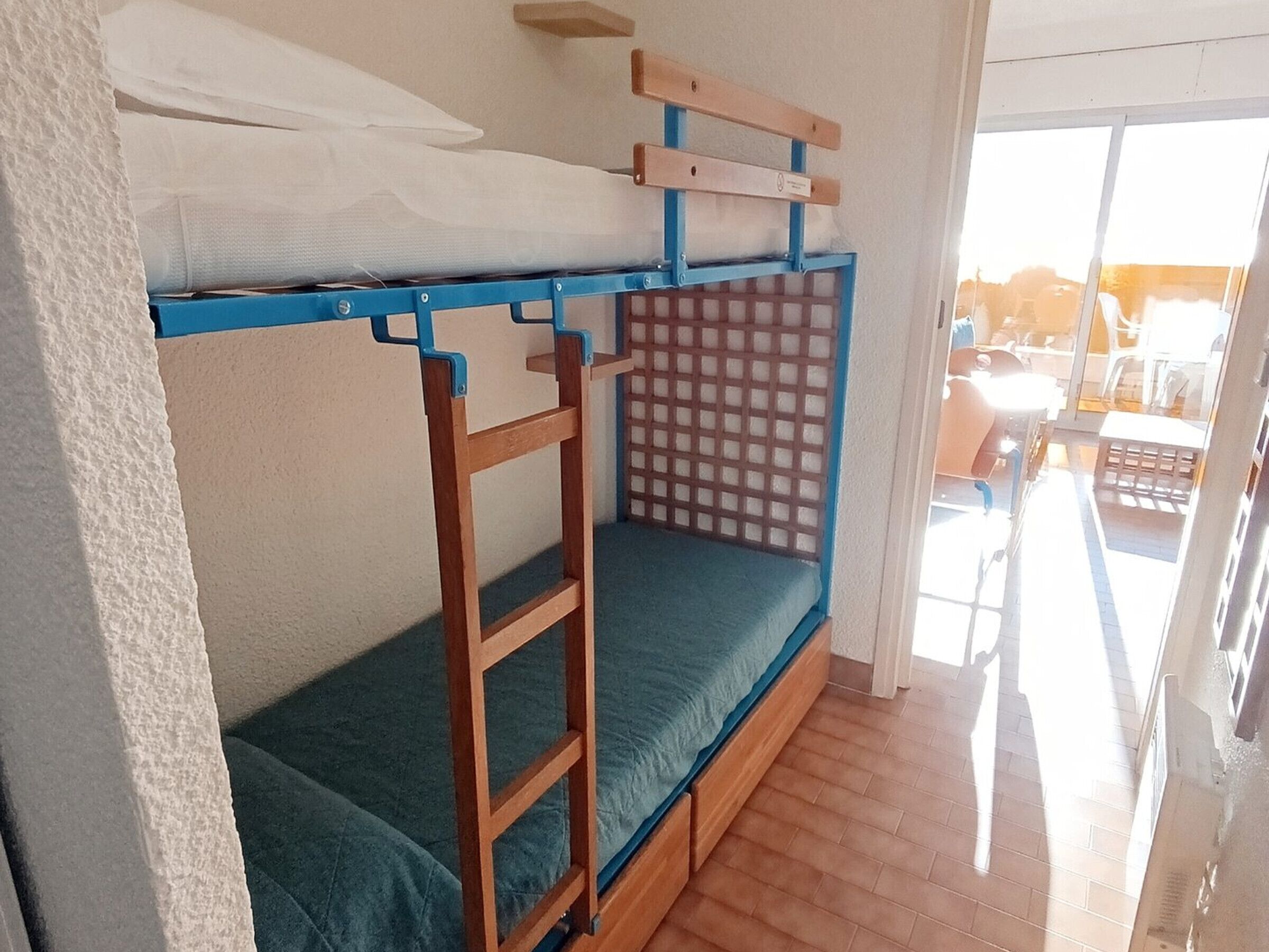 A bunk bed with a wooden frame and a blue mattress, a ladder, and a mesh privacy screen.