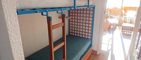 A bunk bed with a wooden frame and a blue mattress, a ladder, and a mesh privacy screen.