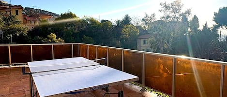 Une table de ping-pong sur un balcon, avec vue sur les arbres et les immeubles.