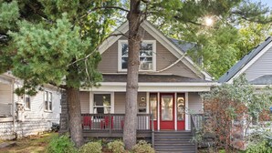 A two-story house with a red front door, a covered front porch, and a large tree in front. - Spacious Home for Groups with Firepit & Backyard (Louisville)
