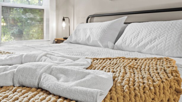 A neatly made bed with white linens and a textured brown throw blanket. - Spacious Home for Groups with Firepit & Backyard (Louisville)