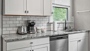 A modern kitchen with white cabinets, a granite countertop, a coffee maker, a toaster, and a dishwasher. - Spacious Home for Groups with Firepit & Backyard (Louisville)