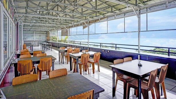 A covered outdoor dining area with tables and chairs, large windows, and a view of the sky and mountains.