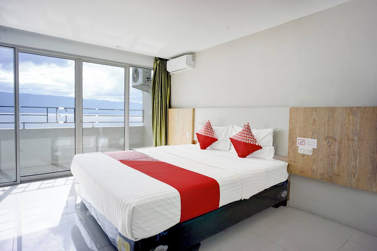 Habitación de hotel con una cama grande, un balcón y vista al mar, y un cabecero de madera.