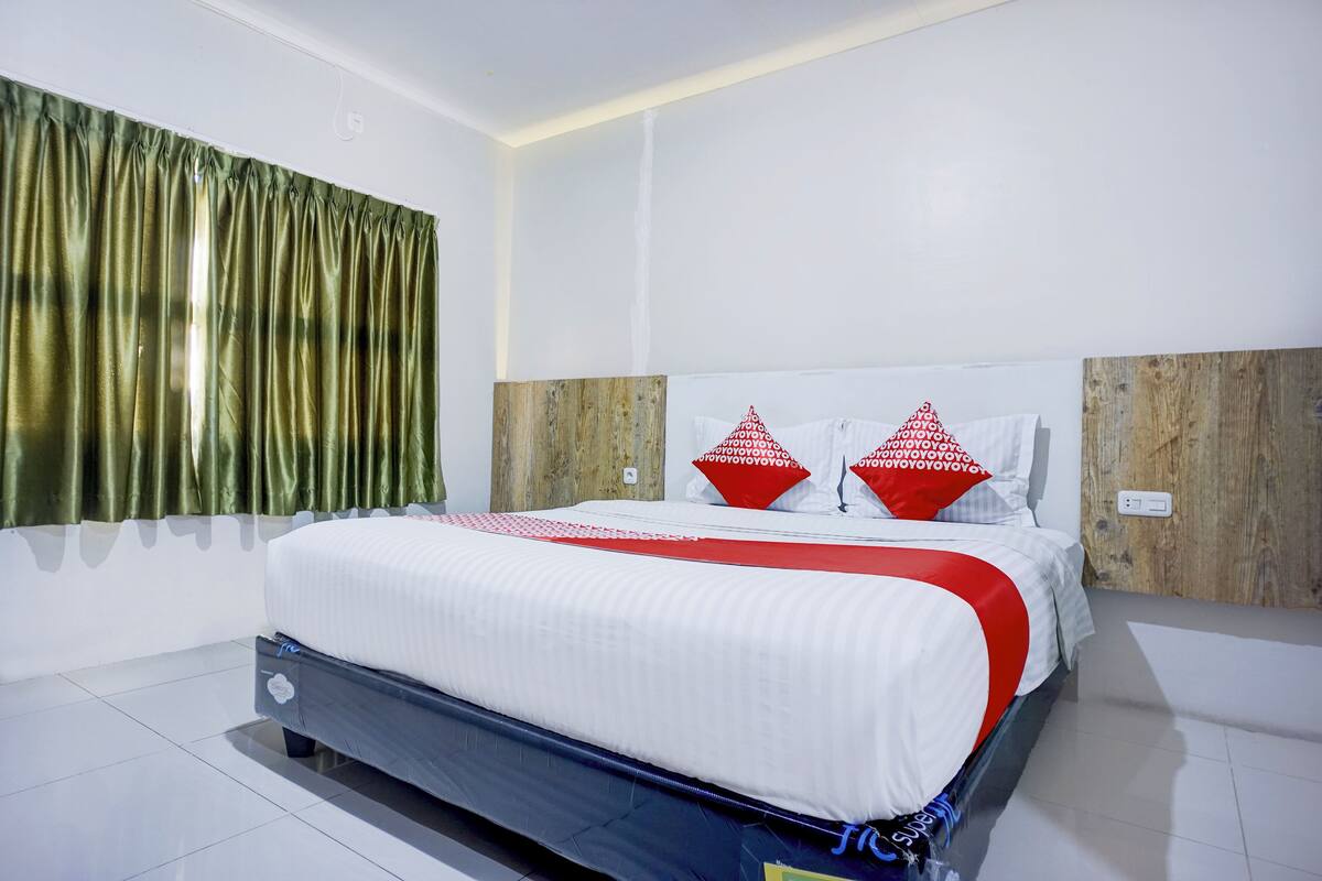 Una cama bien hecha con ropa de cama blanca y roja, un cabecero de madera y una cortina verde.