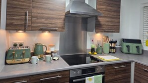 Una cocina moderna con armarios de madera, una campana extractora de acero inoxidable, un horno empotrado y una encimera con diversos electrodomésticos y utensilios.
