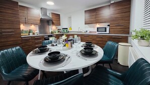 Una cocina moderna con armarios de madera oscura, una encimera blanca y una mesa redonda para cuatro comensales.