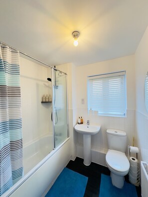 A bathroom with a glass shower enclosure, a white sink, a toilet, and a window with blinds.