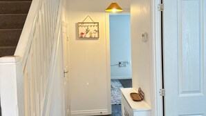 Un pasillo con una escalera, una lámpara colgante, una puerta y una pequeña mesa con un cuenco.