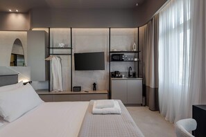 Une chambre d’hôtel moderne dotée d’un grand lit, d’un téléviseur à écran plat fixé au mur, d’une petite kitchenette et d’un coin salon avec un fauteuil.
