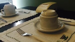 Une table dressée avec deux tasses blanches posées sur des soucoupes, une fourchette et un couteau sur un chemin de table à motifs verts.