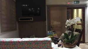 Un hall d’hôtel avec un canapé à motifs, un téléviseur, un comptoir d’accueil et une plante.