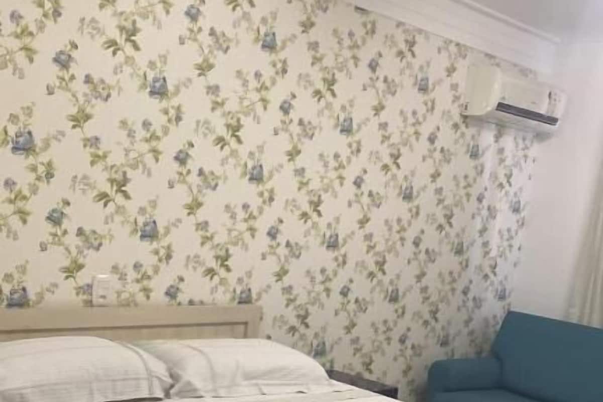Ein ordentlich bezogenes Bett mit einer gestreiften Tagesdecke, ein blaues Sofa und blumiger Wandteppich.
