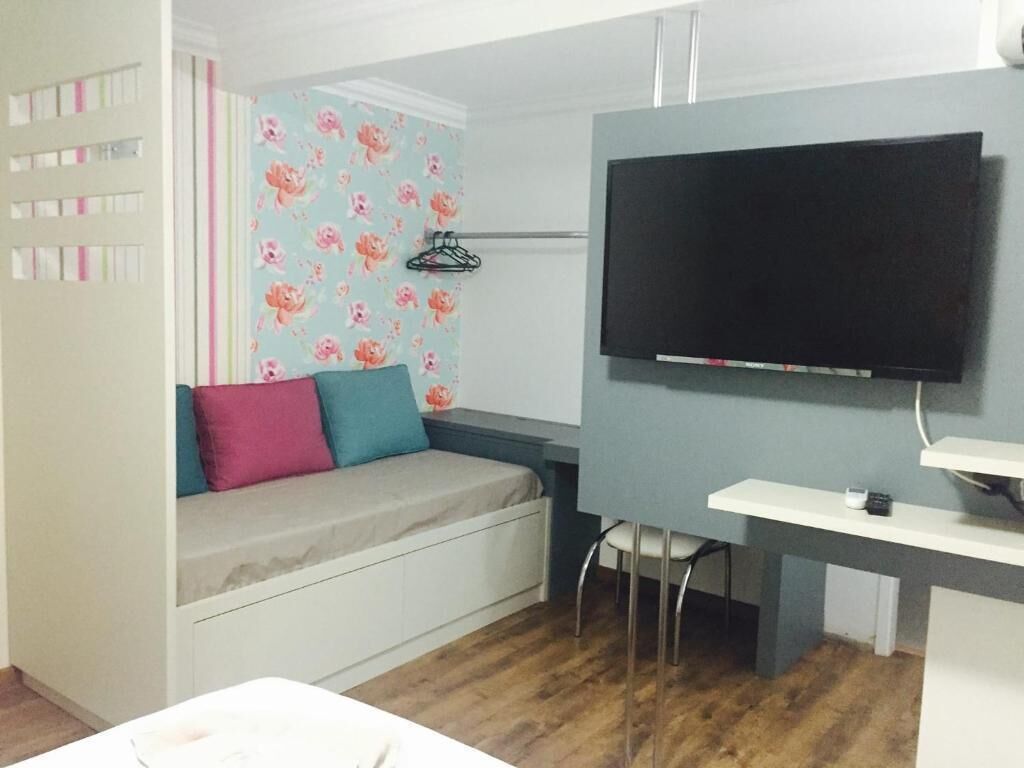 Quarto com cama, televisão na parede, escrivaninha e cadeira.