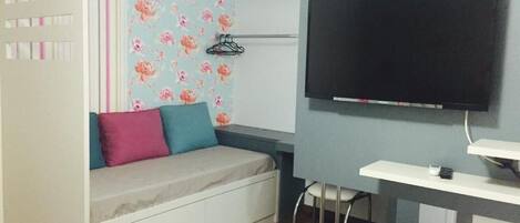 Quarto com cama, televisão na parede, escrivaninha e cadeira.