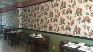 Un restaurant avec un papier peint à motifs floraux, des tables et des chaises en bois.