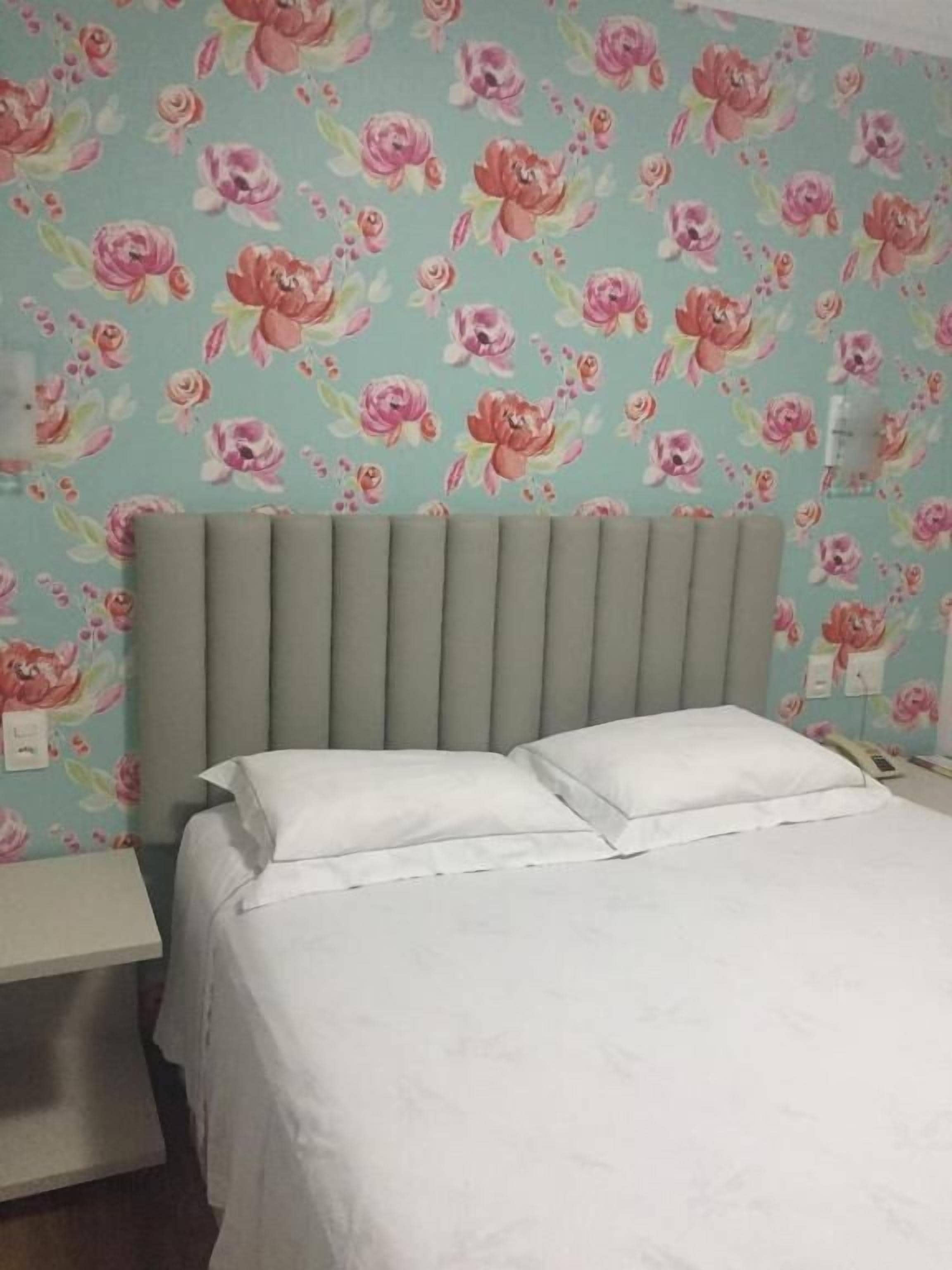 Un lit avec une literie blanche, une tête de lit grise et un papier peint à motifs floraux.