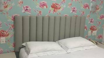 A bed with white bedding, a grey headboard, and a floral wallpaper pattern.