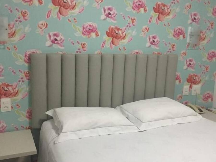 A bed with white bedding, a grey headboard, and a floral wallpaper pattern.