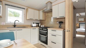 Cocina pequeña con ventana, un lavabo, estufa y comedor con mesa y sillas.