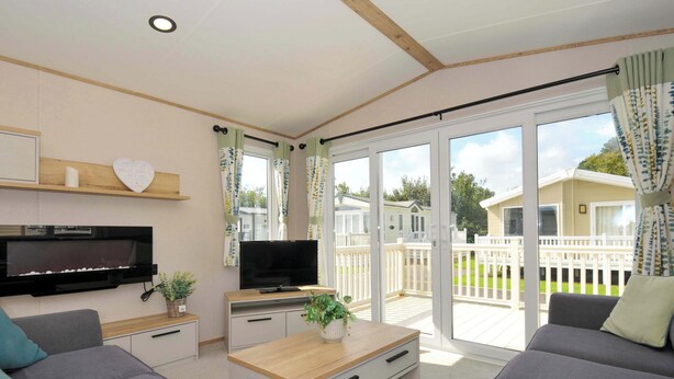 Una sala de estar moderna con una televisión de pantalla plana, sofás grises, una mesa de centro de madera y un gran ventanal corredizo que da a una terraza exterior.