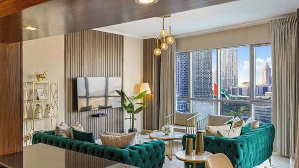 Un salon moderne avec un canapé vert, un téléviseur à écran plat et une vue sur la ville grâce à de grandes fenêtres.