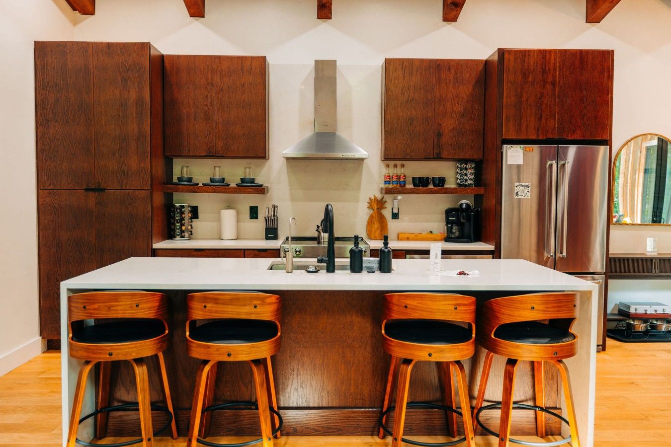 A kitchen with wooden cabinets, a central island with stools, and a stainless steel refrigerator.