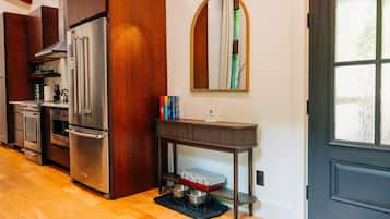 A modern kitchen with stainless steel appliances, a wooden cabinet, a round mirror, and a small table with books.
