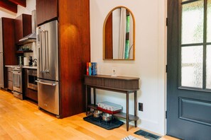 A modern kitchen with stainless steel appliances, a wooden cabinet, a round mirror, and a small table with books.