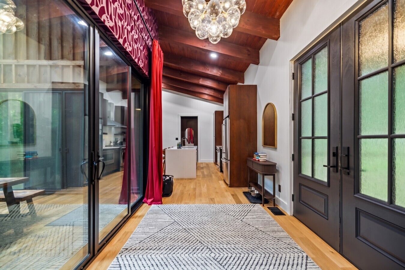 A modern interior with a wooden ceiling, a glass door entrance, a kitchen area, and a dining space.