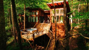 Een houten blokhut met een jacuzzi en een terras, omringd door bomen.