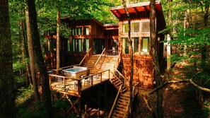 Une cabane en bois dotée d’un bain à remous et d’un espace extérieur aménagé, le tout entouré d’arbres.