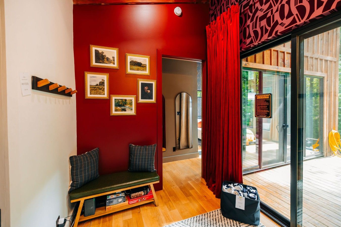 A room with a red wall, a bench with cushions, a shelf with books, and a glass door leading outside.