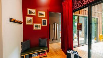 A room with a red wall, a bench with cushions, a shelf with books, and a glass door leading outside.